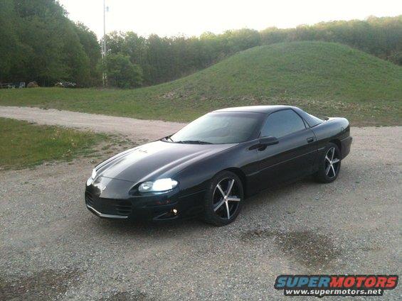 Black 1998 Chevrolet Camaro parked on a gravel road with grassy hills in the background