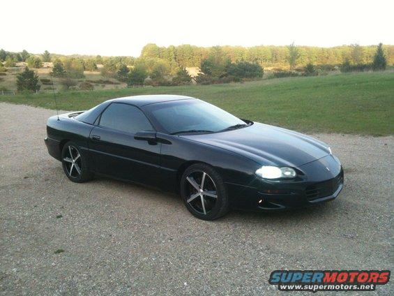 Black 1998 Chevrolet Camaro parked on a gravel road with trees and hills in the background