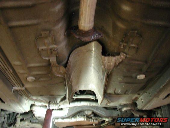 Underside view of a car's exhaust system and undercarriage. Shows the catalytic converter area and part of the exhaust pipe