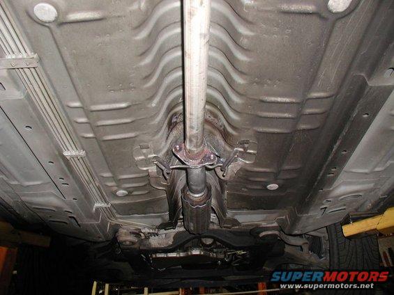Underside of a vehicle showing the exhaust system and catalytic converter. The vehicle is viewed from below, angled slightly towards the front