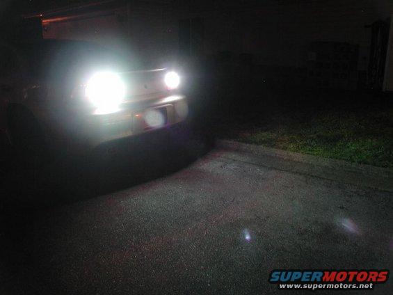 Car front with bright headlights on at night, asphalt and grass visible