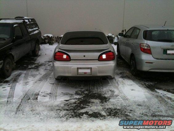 Rear view of a silver 2002 Pontiac Grand Prix parked in snow, with a black truck and silver hatchback nearby