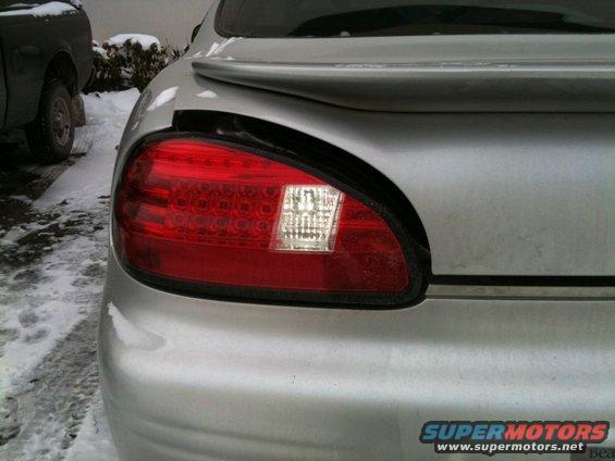 Silver car's damaged rear tail light assembly. Snow on the ground and another vehicle visible