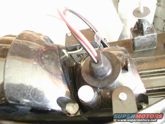 Close-up of a car part with red and black wires connected to a black plastic housing; 'SUPERMOTORS' logo visible