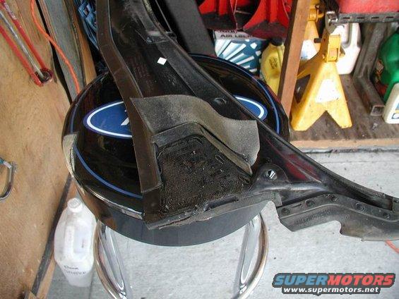 Black plastic car part with mesh and foam, resting on a black helmet with a blue Ford logo