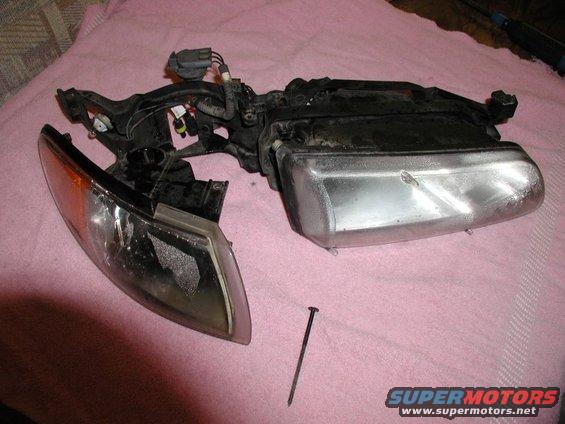 Car headlight assembly with orange turn signal lens and clear main lens, resting on a pink cloth. A nail is on the cloth next to it