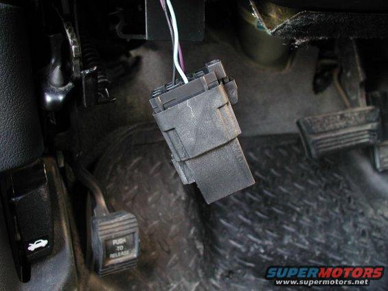 Wiring harness connector hanging near brake and gas pedals. Hood release lever visible