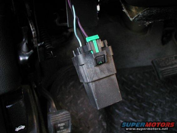 Close-up of a black electrical connector with green and purple wires, near a pedal with 'PUSH TO RELEASE' text