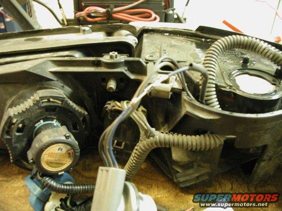 Close-up of a car headlight assembly with wiring and a circular component with text