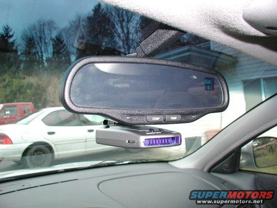 Radar detector mounted below rearview mirror, with a white car and red truck visible through the windshield