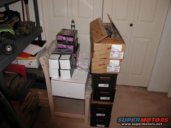 Stack of car part boxes, including TYC and Monroe brands, on a chair next to shelves with other items