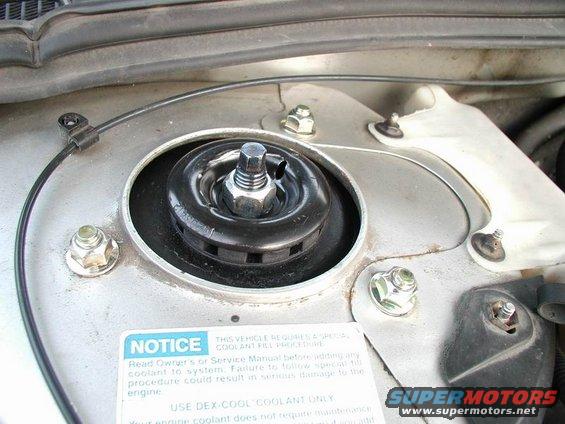 Close-up of a car's strut mount with a notice sticker about coolant