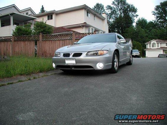 Silver sedan parked on asphalt driveway, front 3/4 view. Houses and trees in background