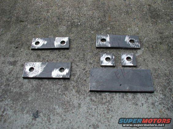 Several metal brackets and plates with drilled holes on a concrete surface