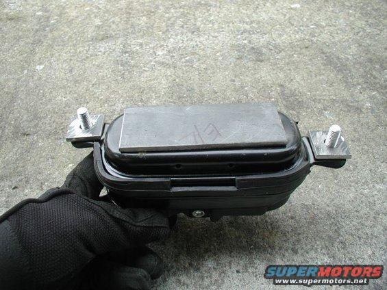 Black automotive part with metal plate and bolts, held by gloved hand