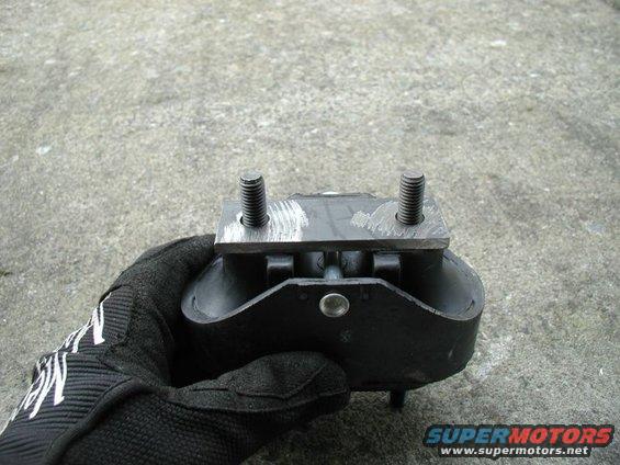 Black engine mount with two bolts, held in a gloved hand