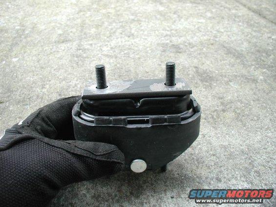 Gloved hand holding a black engine mount with two threaded studs