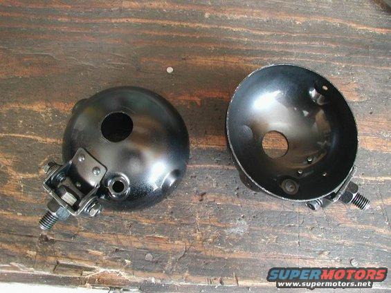 Two black headlight housings with mounting hardware, resting on a wooden surface