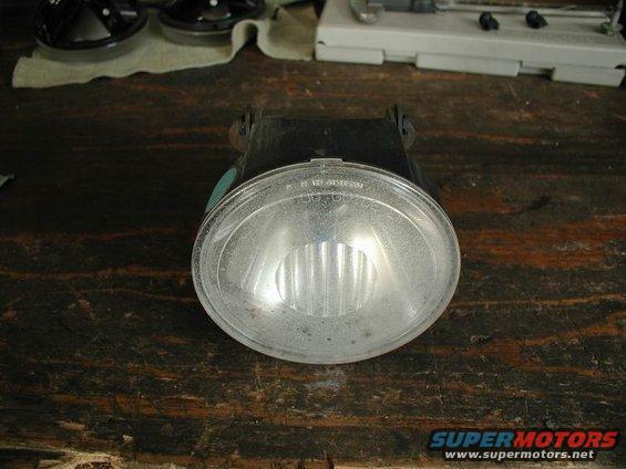 Fog light assembly with clear lens and black housing, resting on a wooden surface