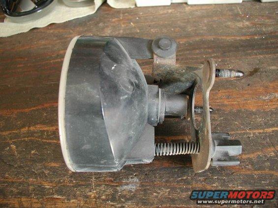 Automotive fog light assembly with black housing and metal bracket, resting on a wooden surface