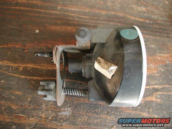 Automotive fog light assembly with mounting bracket and springs, resting on a wooden surface. A sticker is affixed to the housing