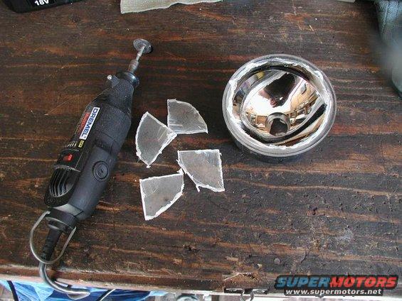 Broken fog light with Dremel tool and glass shards on wooden surface