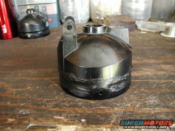 Black car headlight assembly with clear lens and internal reflector, resting on a wooden surface