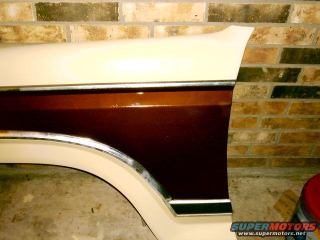 Close-up of a vehicle's fender and wheel well, showing two-tone paint and chrome trim
