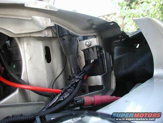 Close-up of silver metal bracket with black wiring and red cables, part of a vehicle's electrical system
