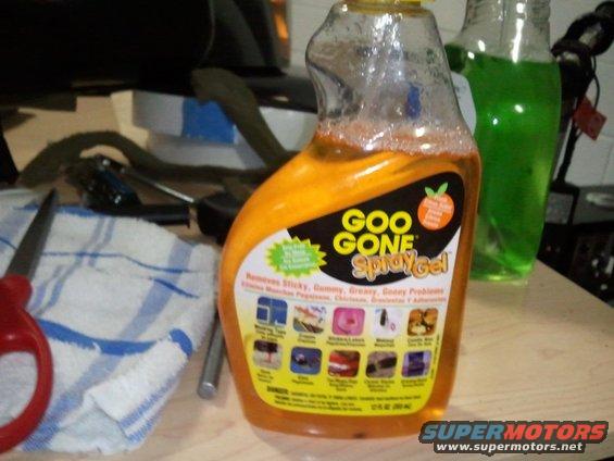 Bottle of orange Goo Gone spray gel with label showing various cleaning applications, next to scissors and a towel