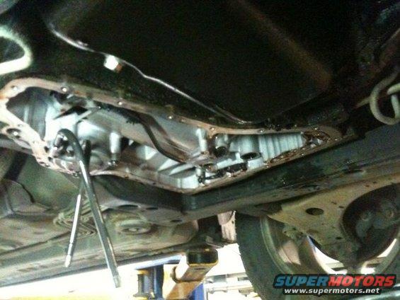 Transmission pan with gasket removed, showing internal components and tools. Underside of a vehicle