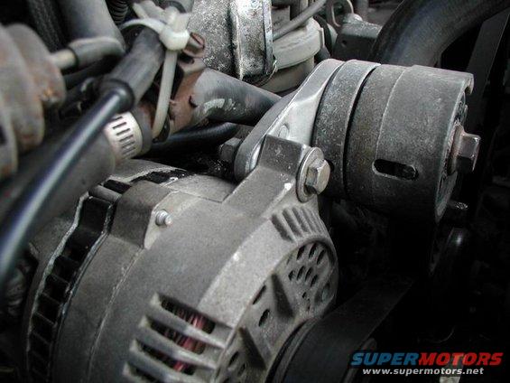 Close-up of an automotive alternator with hoses and belts visible
