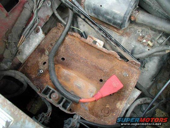 Close-up of a heavily rusted battery tray with orange cable and black wiring in an engine bay