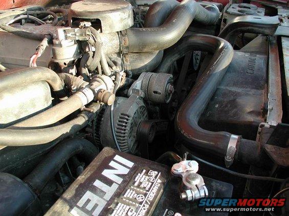Engine bay showing alternator, hoses, and battery. Text on battery reads 'INTER'