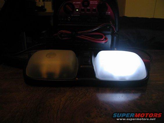 Two vehicle dome lights, one yellow and one bright white, sit in front of a battery charger