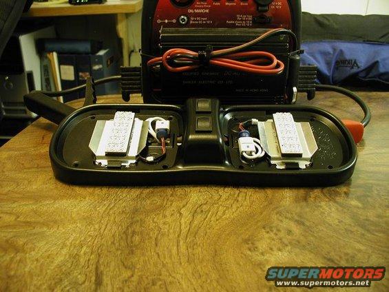 Disassembled interior dome light assembly with wiring and circuit boards visible, next to a battery charger