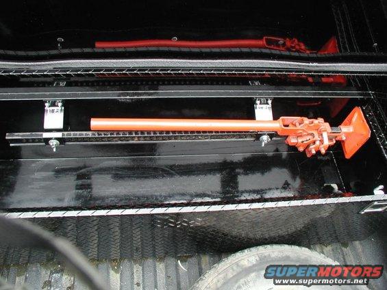 Orange Hi-Lift jack mounted on a black rack inside a truck bed