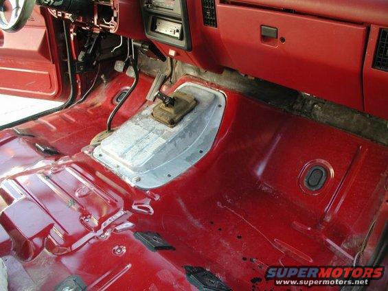 Red truck interior with floor stripped bare, showing transmission tunnel and pedals