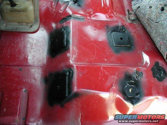 Red floor pan with black patches covering holes, possibly for seat mounts