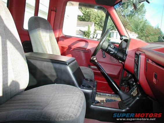 Red truck interior with grey cloth seats, black center console, and floor shifter. Visible text 'SUPERMOTORS'