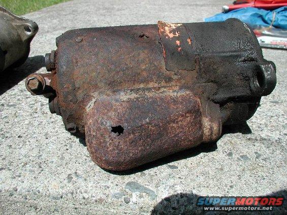 Rusted starter motor with visible hole and orange paint flecks