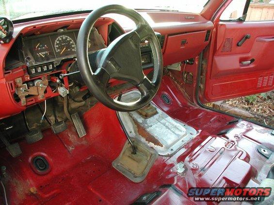 Interior of a red 1990 Ford F-250 showing steering wheel, dashboard, and floor