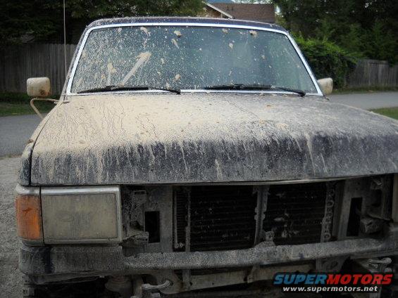 mud-splattered truck front end, grille missing, headlights visible