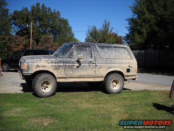 1990 Ford Bronco covered in mud, parked on grass