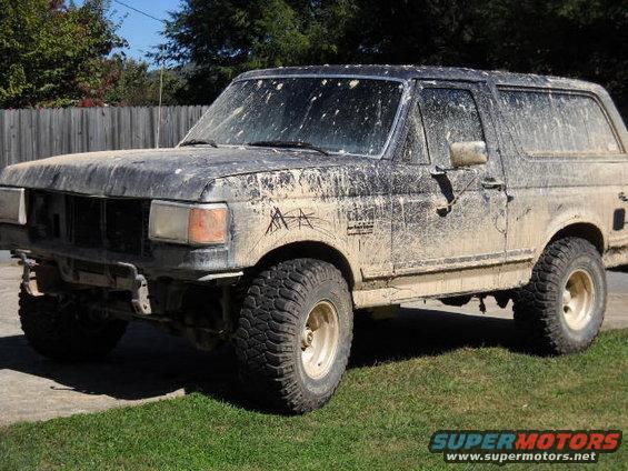 Mud-caked SUV parked on grass. Front bumper is missing and the vehicle is covered in dirt splatters
