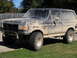 1990 Ford Bronco - This SUV is heavily coated in mud, obscuring much of its original appearance.