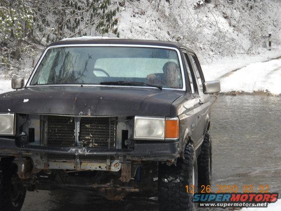 1990 Ford Bronco front view, missing grille, in snow. Water in foreground