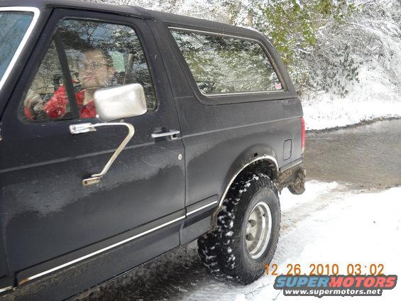 Side view of a black 1990 Ford Bronco in the snow, driver visible inside