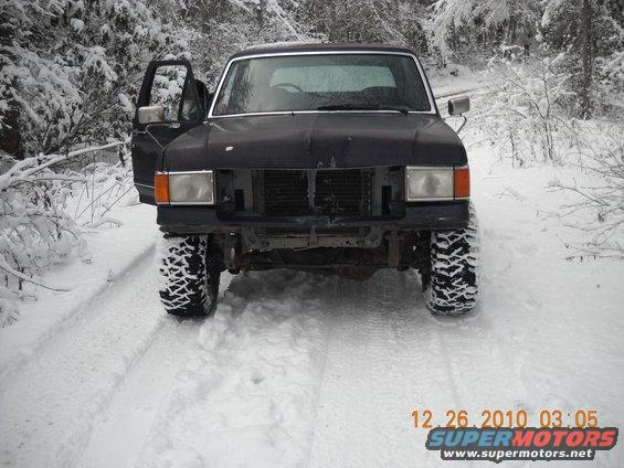 Black Ford Bronco with open driver door, off-road tires, in snowy woods