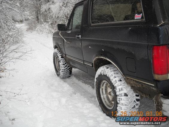 Black Ford Bronco on a snowy road, tires covered in snow. A sticker is on the rear window